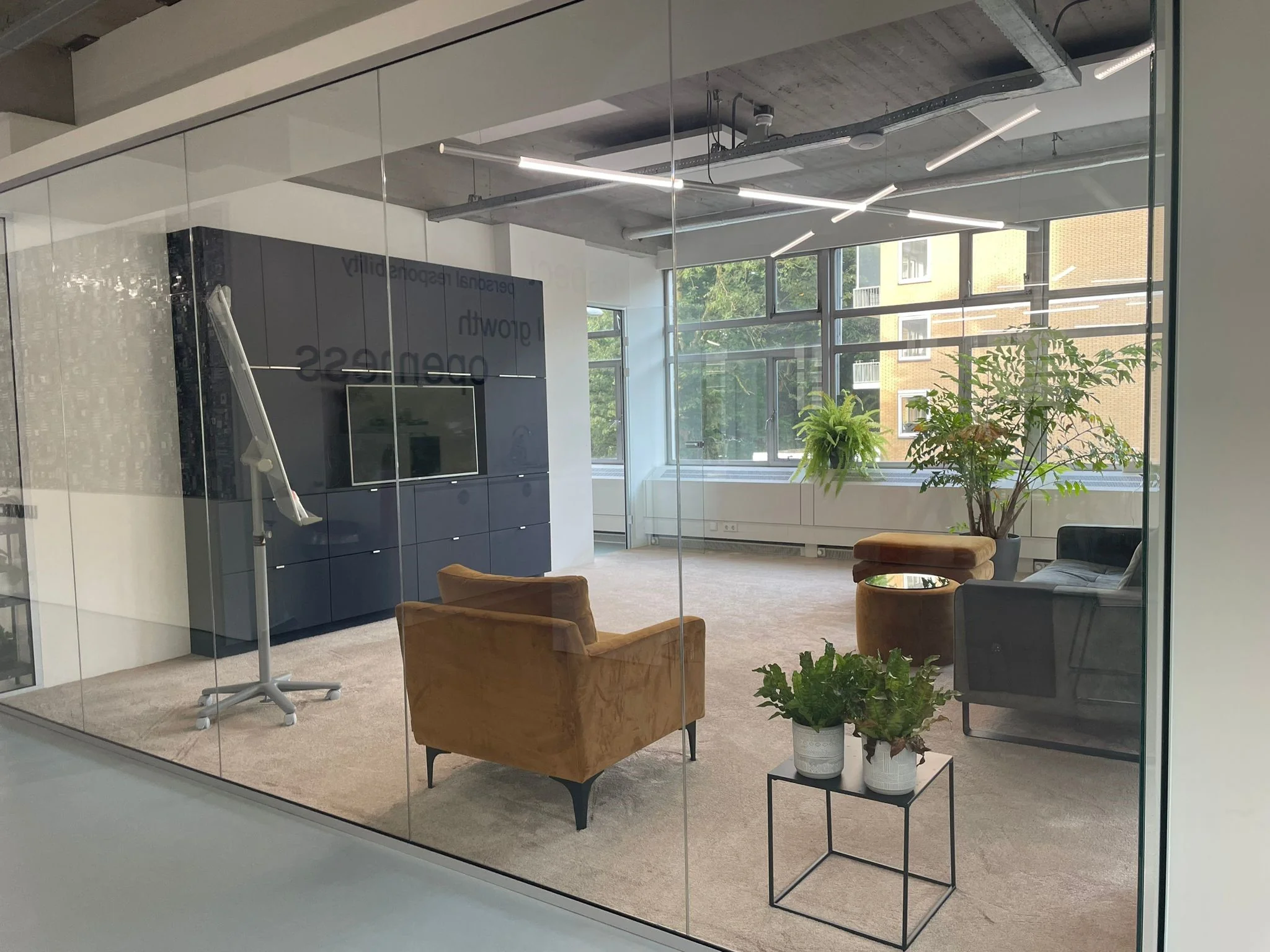 Modern ingerichte vergaderruimte aan de Van Leijenberghlaan met glazen wanden, comfortabele zitmeubels, veel lichtinval en diverse planten.